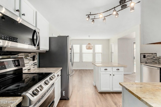 kitchen with appliances with stainless steel finishes, white cabinetry, backsplash, light stone counters, and light hardwood / wood-style flooring