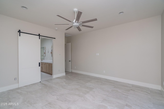 unfurnished bedroom featuring a barn door, ceiling fan, and ensuite bathroom