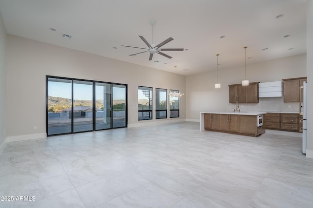 kitchen with sink, hanging light fixtures, a high ceiling, tasteful backsplash, and an island with sink