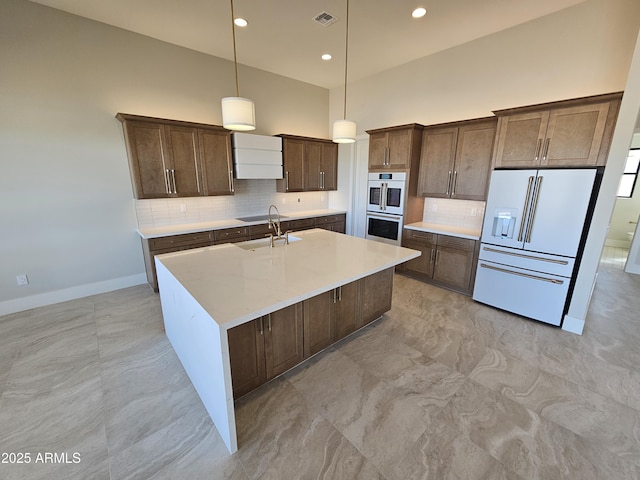 kitchen with white appliances, a kitchen island with sink, hanging light fixtures, a high ceiling, and tasteful backsplash