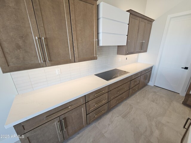 kitchen featuring light stone countertops, dark brown cabinets, backsplash, and black electric cooktop