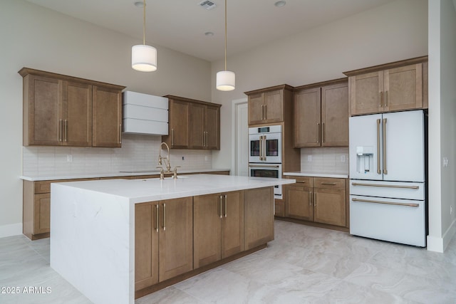 kitchen with decorative light fixtures, tasteful backsplash, sink, a kitchen island with sink, and white appliances