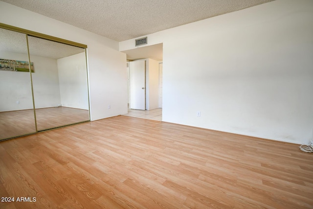 unfurnished bedroom featuring a textured ceiling, light hardwood / wood-style floors, and a closet