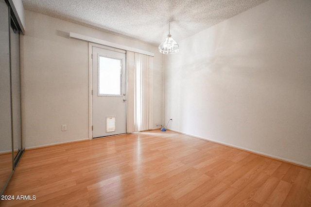 empty room with an inviting chandelier, light hardwood / wood-style floors, and a textured ceiling