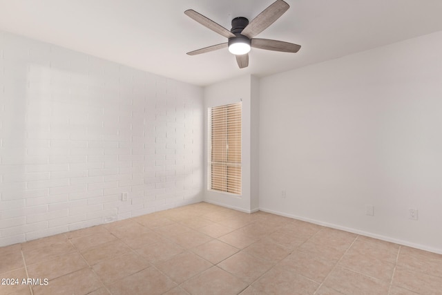 unfurnished room with ceiling fan, light tile patterned floors, and brick wall