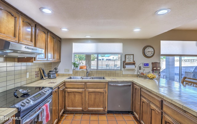 kitchen with tile countertops, sink, light tile patterned floors, kitchen peninsula, and stainless steel appliances