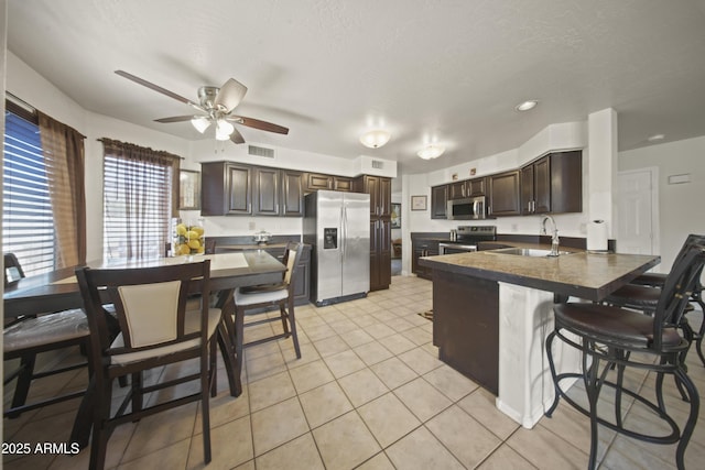 13160 W Windsor Ave, Goodyear, AZ 85395 - kitchen with appliances with stainless steel finishes, dark brown cabinets, a peninsula, a ceiling fan, and a breakfast bar