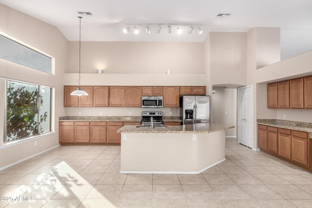 kitchen featuring sink, an island with sink, decorative light fixtures, light stone counters, and stainless steel appliances