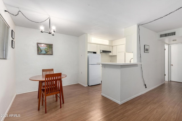 kitchen featuring white cabinets, white refrigerator, hardwood / wood-style flooring, kitchen peninsula, and an inviting chandelier