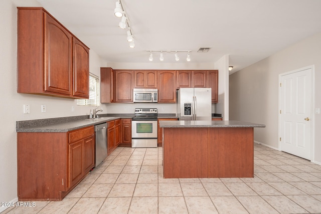 kitchen with rail lighting, stainless steel appliances, sink, light tile patterned floors, and a center island