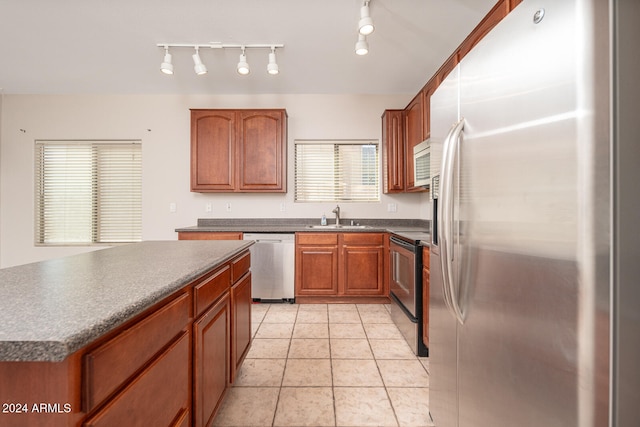 kitchen featuring appliances with stainless steel finishes, rail lighting, sink, light tile patterned floors, and a kitchen island