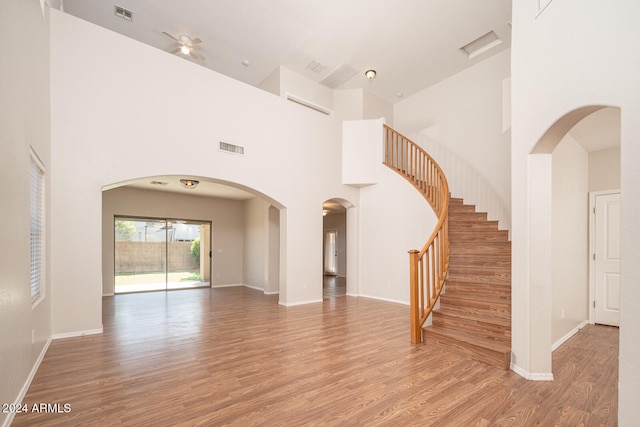 unfurnished living room featuring ceiling fan, wood-type flooring, and a high ceiling