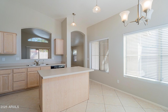 kitchen featuring arched walkways, light countertops, light brown cabinets, a sink, and light tile patterned flooring