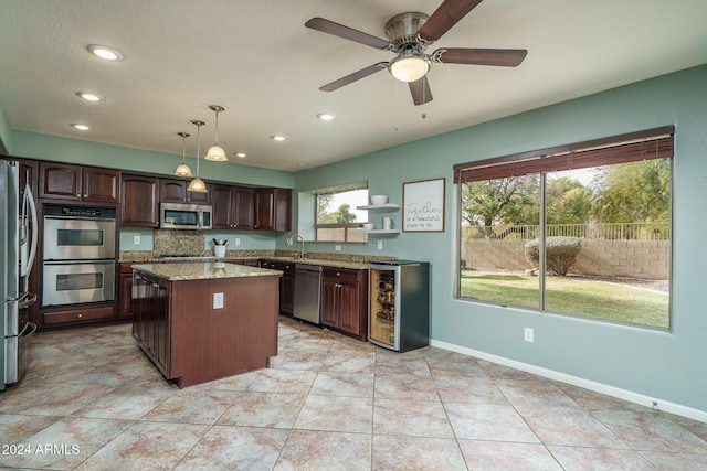 kitchen featuring appliances with stainless steel finishes, dark brown cabinets, beverage cooler, a kitchen island, and hanging light fixtures