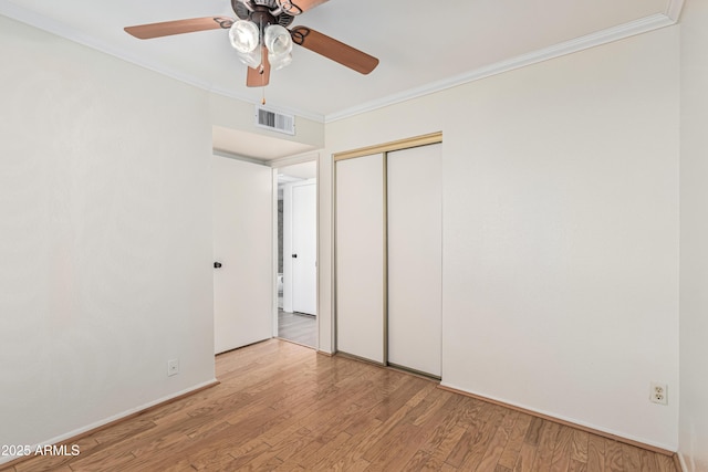 unfurnished bedroom with light wood-type flooring, ceiling fan, a closet, and crown molding