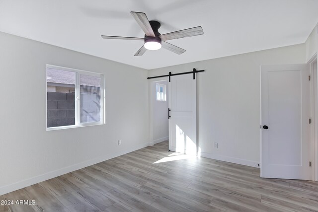 unfurnished room with light wood-type flooring, a barn door, and ceiling fan