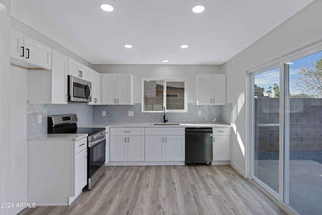 kitchen with white cabinets, sink, light hardwood / wood-style flooring, decorative backsplash, and stainless steel appliances