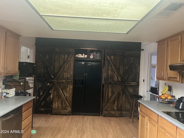 kitchen with black appliances, a barn door, and light hardwood / wood-style flooring