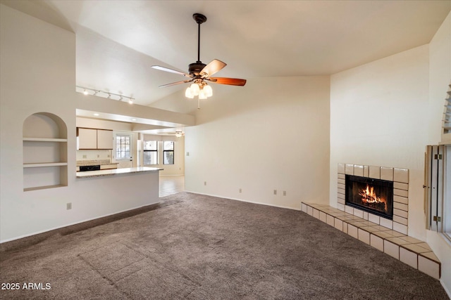 unfurnished living room with carpet floors, built in shelves, vaulted ceiling, ceiling fan, and a tile fireplace