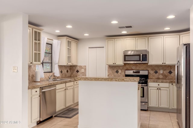 kitchen featuring sink, stainless steel appliances, light tile patterned floors, cream cabinets, and a kitchen island