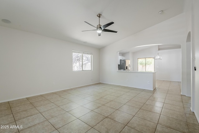 unfurnished room featuring a ceiling fan, plenty of natural light, arched walkways, light tile patterned floors, and vaulted ceiling