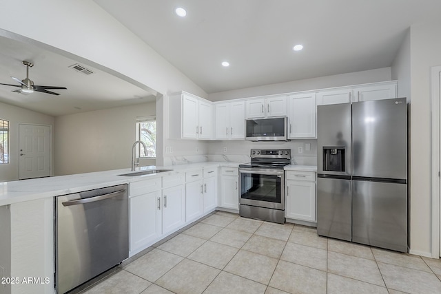 kitchen with a peninsula, white cabinetry, a sink, vaulted ceiling, and stainless steel appliances