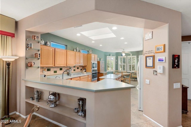 kitchen featuring stainless steel appliances, a skylight, kitchen peninsula, light brown cabinetry, and tasteful backsplash