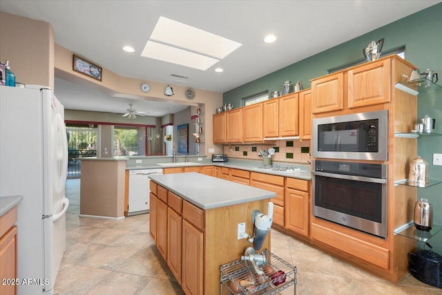 kitchen with white appliances, kitchen peninsula, a center island, a skylight, and sink