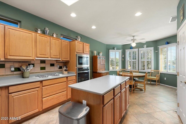 kitchen with stainless steel appliances, light tile patterned flooring, ceiling fan, backsplash, and a kitchen island