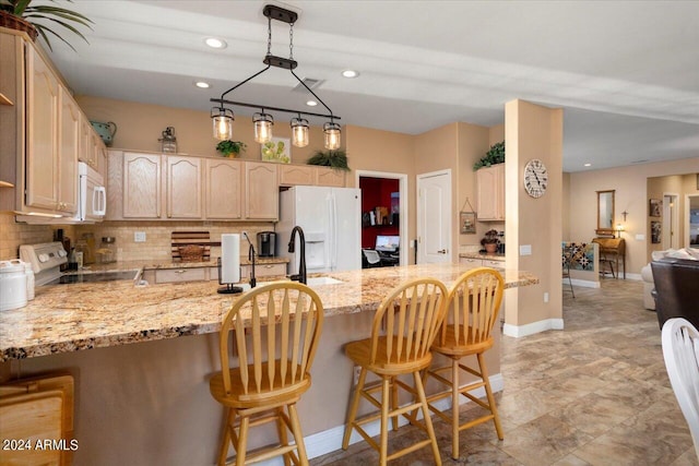 kitchen featuring light brown cabinetry, a kitchen bar, white appliances, and kitchen peninsula