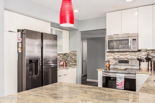 kitchen with tasteful backsplash, modern cabinets, appliances with stainless steel finishes, light stone countertops, and white cabinetry