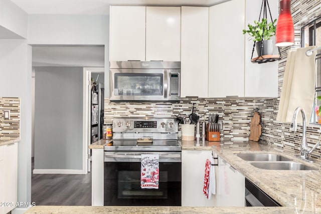 kitchen with stainless steel appliances, white cabinetry, a sink, and light stone countertops