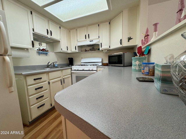 kitchen featuring white appliances, a skylight, sink, and kitchen peninsula