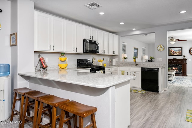 907 E Kelsi Ave, San Tan Valley, AZ 85140 - kitchen with black appliances, a peninsula, recessed lighting, white cabinetry, and a breakfast bar