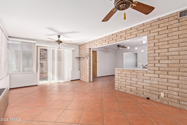 tiled spare room featuring ceiling fan and brick wall