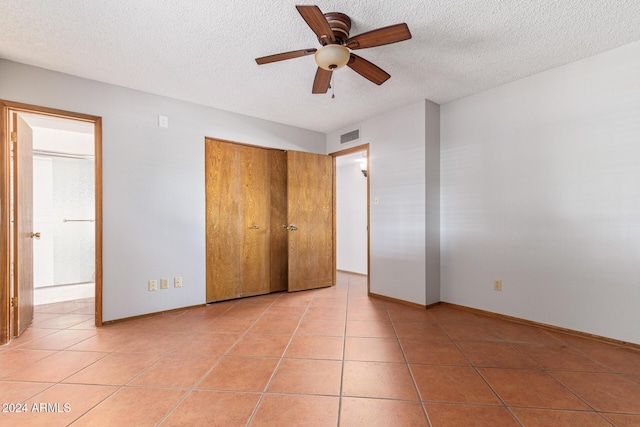 unfurnished bedroom with ceiling fan, light tile patterned floors, a textured ceiling, and ensuite bath