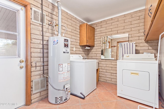 laundry area featuring washer and clothes dryer, cabinets, brick wall, gas water heater, and light tile patterned flooring