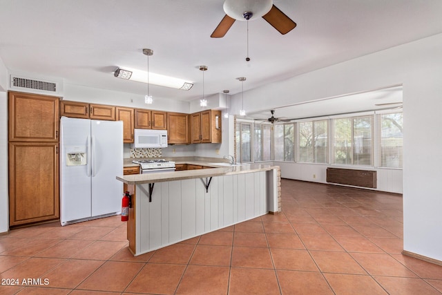 kitchen with sink, white appliances, hanging light fixtures, a kitchen bar, and kitchen peninsula