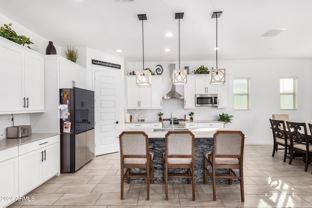 kitchen with pendant lighting, a kitchen island with sink, and wall chimney exhaust hood