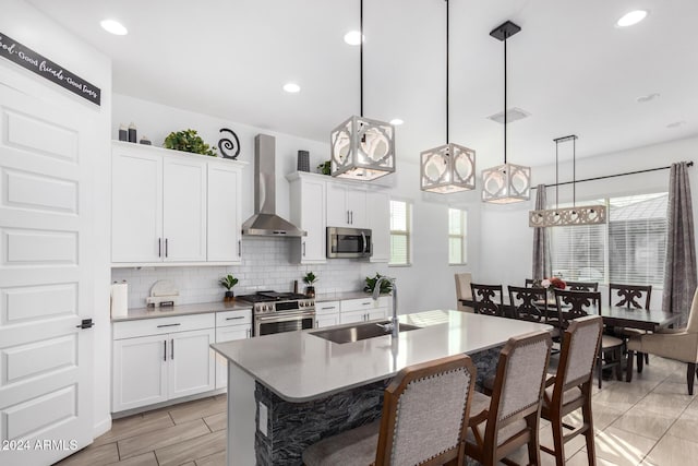 kitchen with sink, wall chimney exhaust hood, decorative light fixtures, white cabinetry, and stainless steel appliances