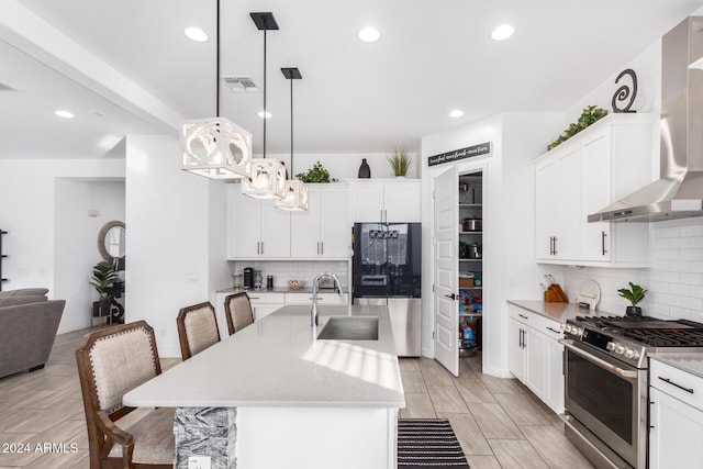 kitchen with sink, hanging light fixtures, wall chimney range hood, a center island with sink, and appliances with stainless steel finishes