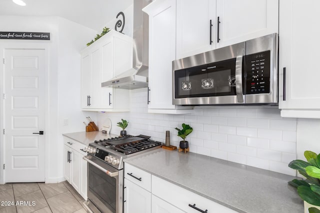 kitchen with decorative backsplash, stainless steel appliances, wall chimney range hood, light tile patterned floors, and white cabinetry