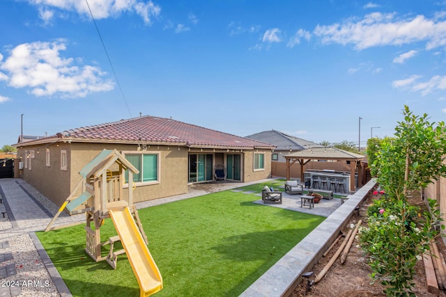 rear view of house with a yard, a playground, an outdoor living space with a fire pit, a gazebo, and a patio area