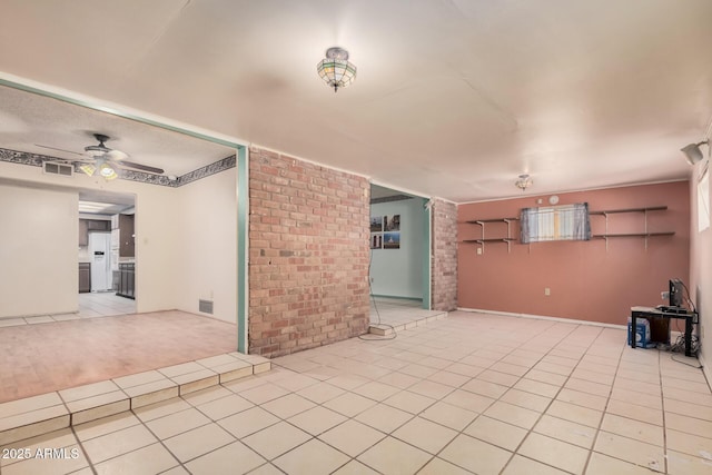 unfurnished living room featuring light tile patterned floors, ceiling fan, and brick wall