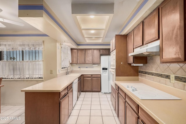 kitchen featuring kitchen peninsula, white appliances, a raised ceiling, sink, and light tile patterned floors