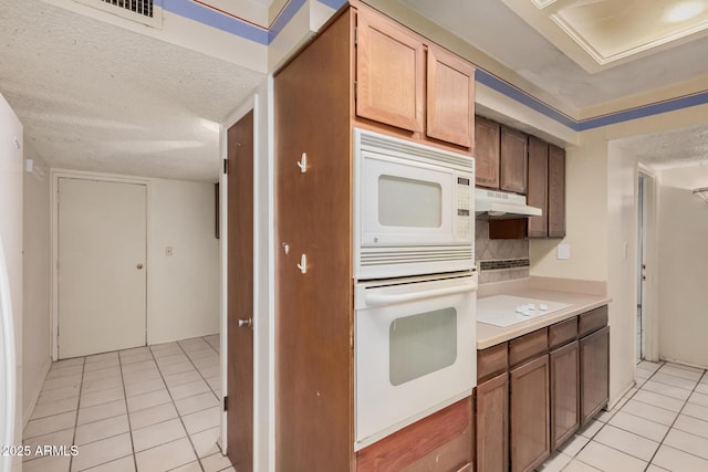 kitchen featuring light tile patterned flooring, white appliances, and a textured ceiling