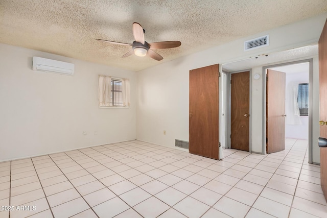 unfurnished room with an AC wall unit, ceiling fan, light tile patterned floors, and a textured ceiling