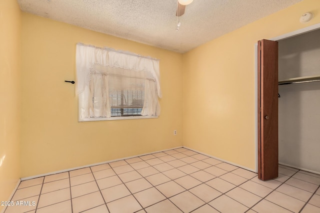 unfurnished bedroom with ceiling fan, a closet, light tile patterned flooring, and a textured ceiling