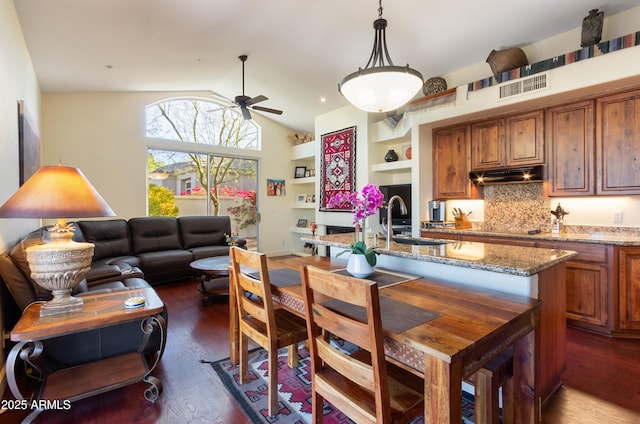 kitchen featuring ceiling fan, light stone counters, dark hardwood / wood-style flooring, lofted ceiling, and decorative backsplash