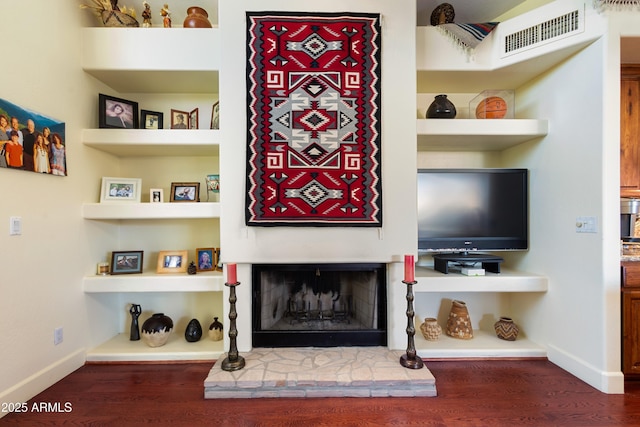 living room with built in shelves, a stone fireplace, and wood-type flooring